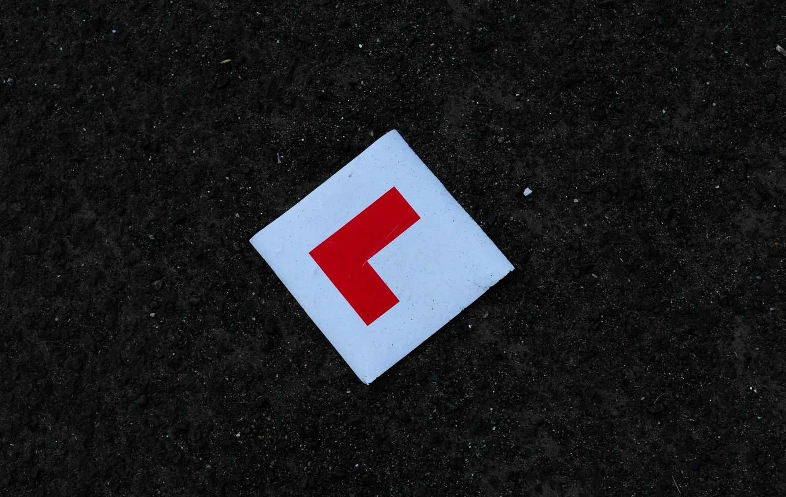 Red L learner driver plate lying on dark asphalt